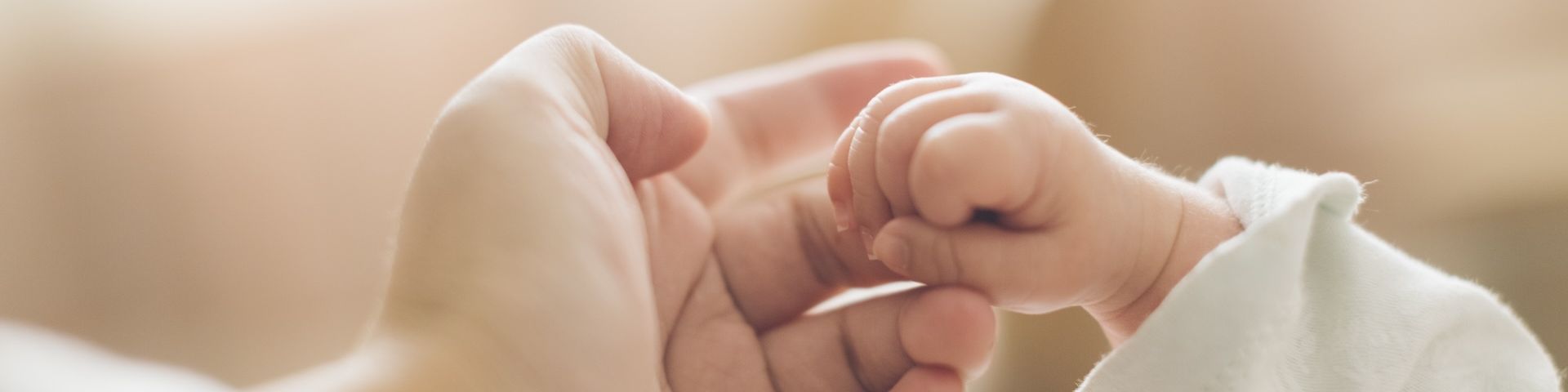 Eine erwachsene Hand hält die eines Neugeborenen.