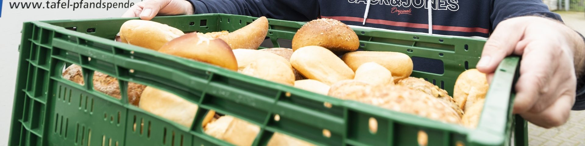 Ein Mitarbeiter der Tafel präsentiert eine Kiste mit Brötchen.