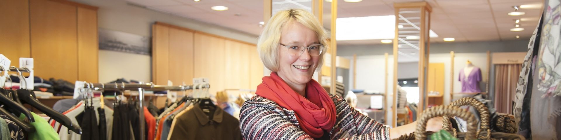 Eine blonde Frau steht im Lüttje Knippke und sortiert Kleidung.