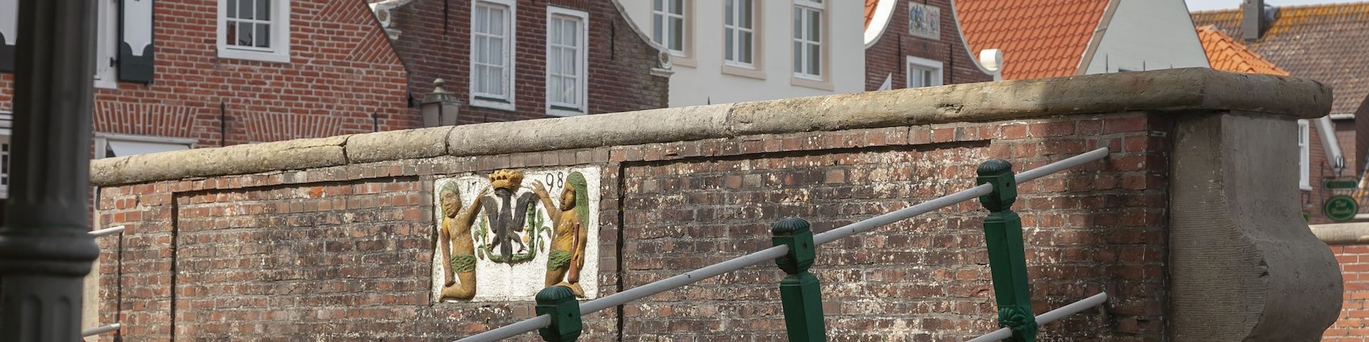 Eine gemauerte Brücke mit Wappen. Dahinter typische Leeraner Häuser.