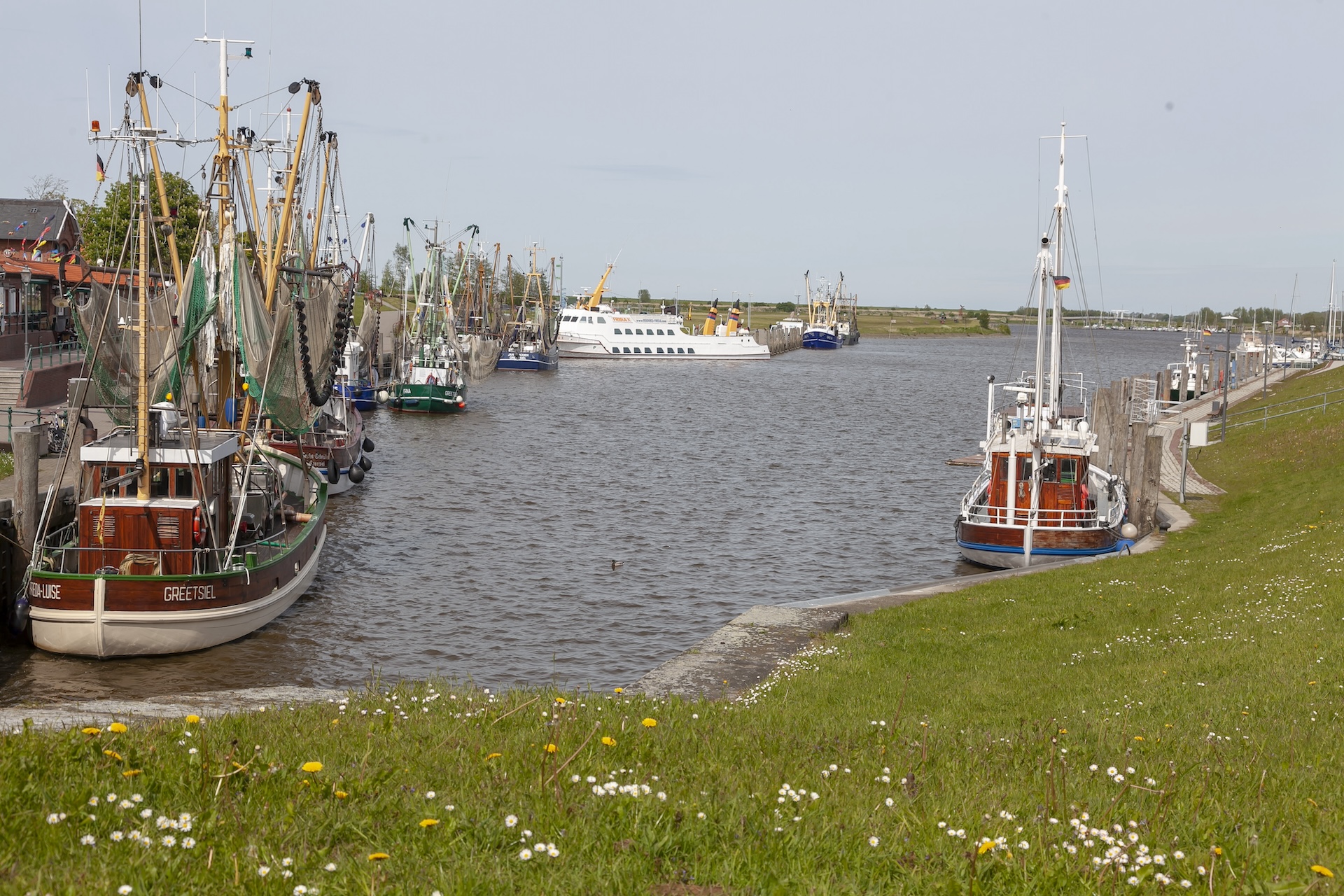 Vertäute Fischerboote am begrünten Ufer.